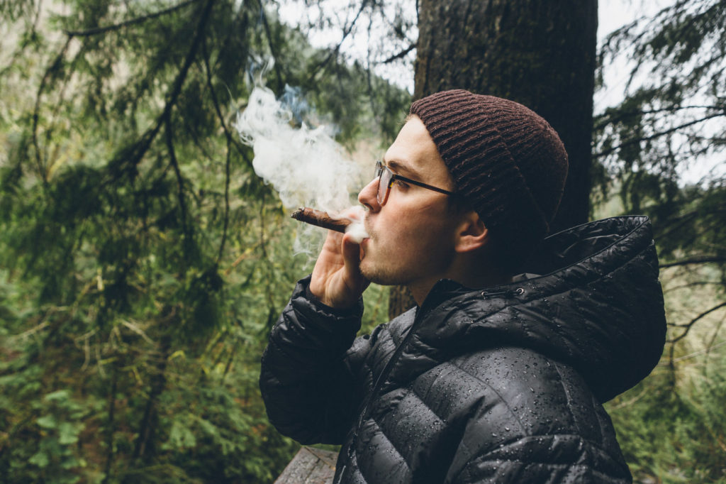 Young Man Smoking Cigar Outside In Forest Air